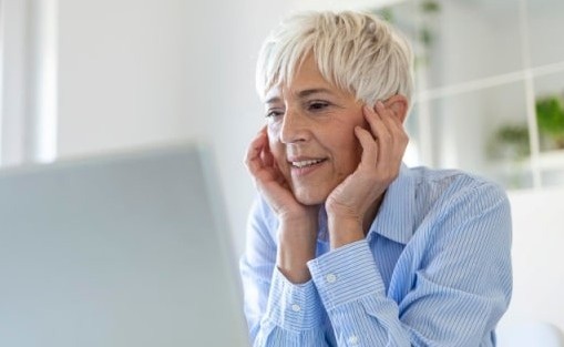 Google ads A woman with grey hair and a blue shirt sitting at a table looking at a laptop computer.